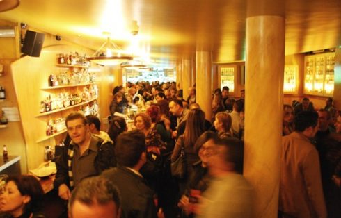 El interior del bar lleno de gente de pie junto a la barra y las columnas