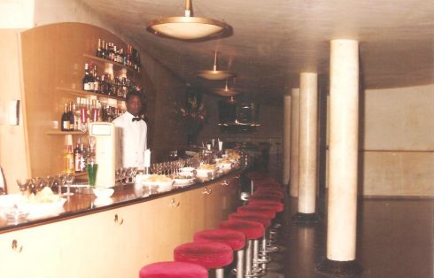 La barra con taburetes rojos y el camarero tras el mostrador