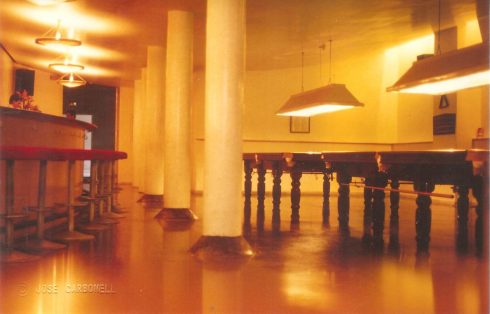 Las mesas de billar bajo las lámparas colgantes, con las columnas y la barra a la izquierda